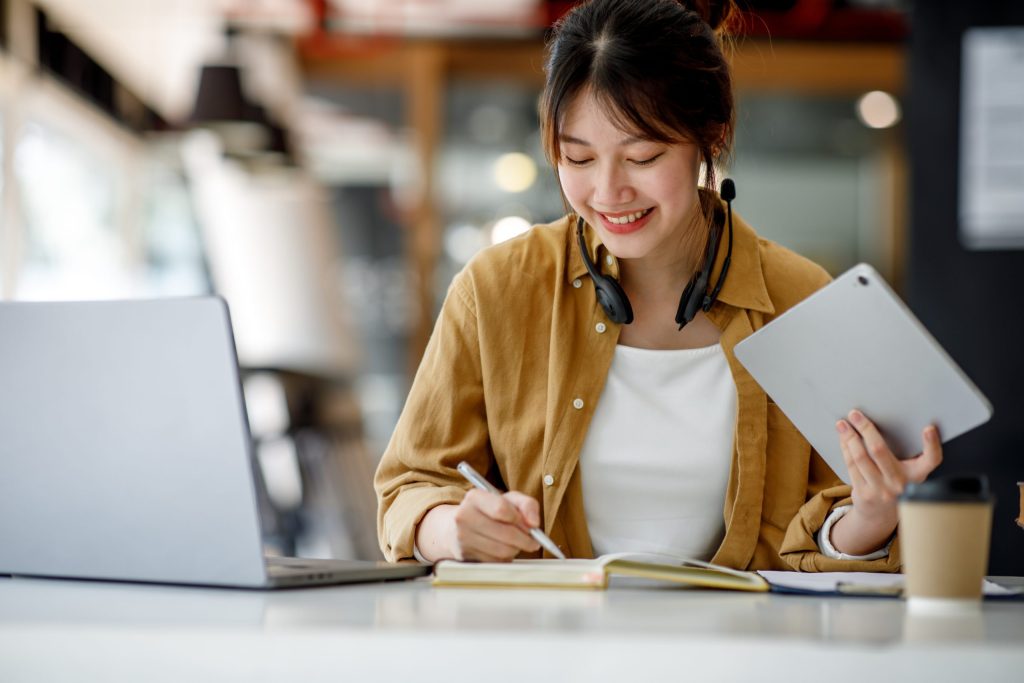 Student attending H2 Math tuition in Singapore, studying with a tablet and laptop while taking notes to improve problem-solving skills.
