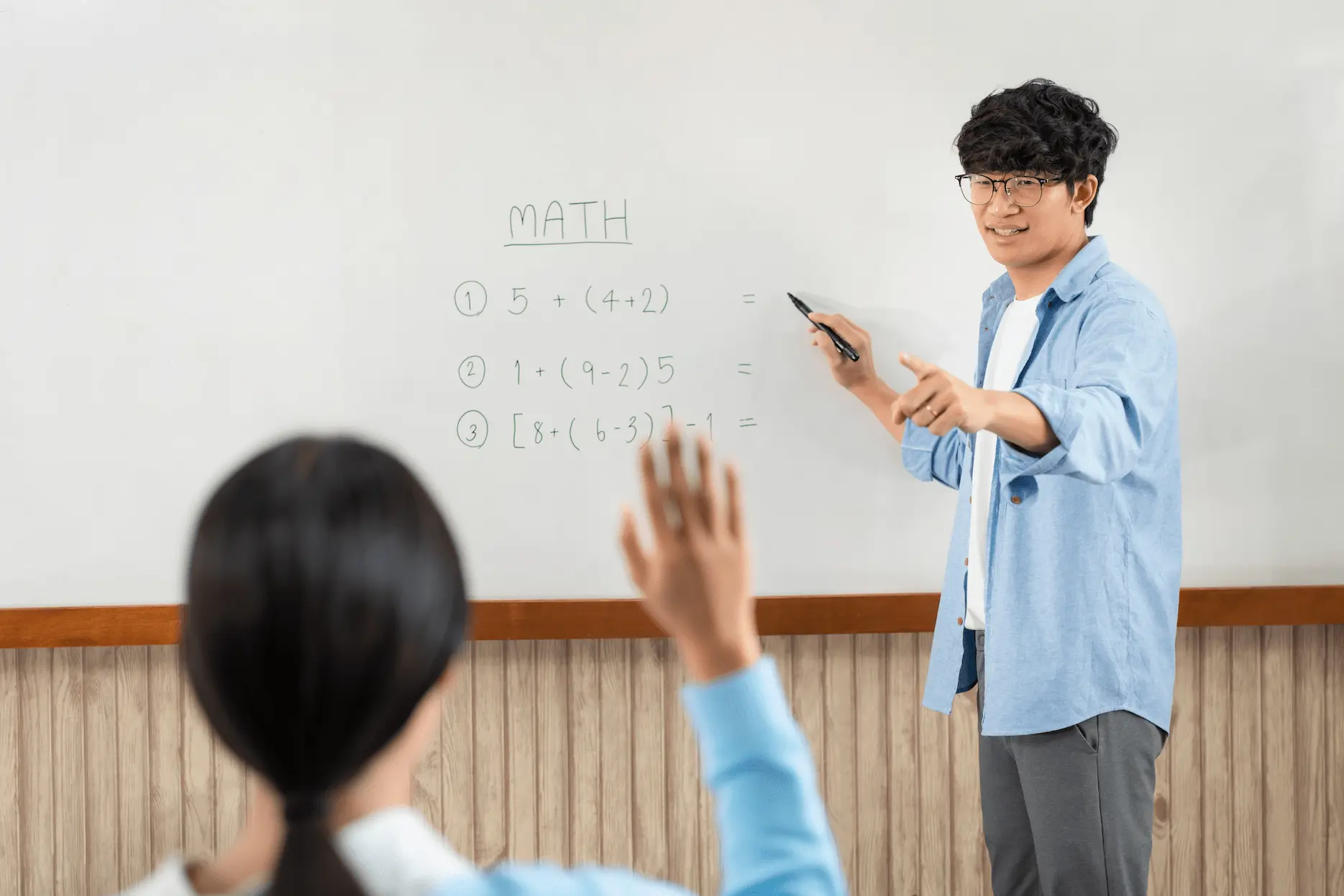 male-tutor-standing-front-whiteboard-pointing