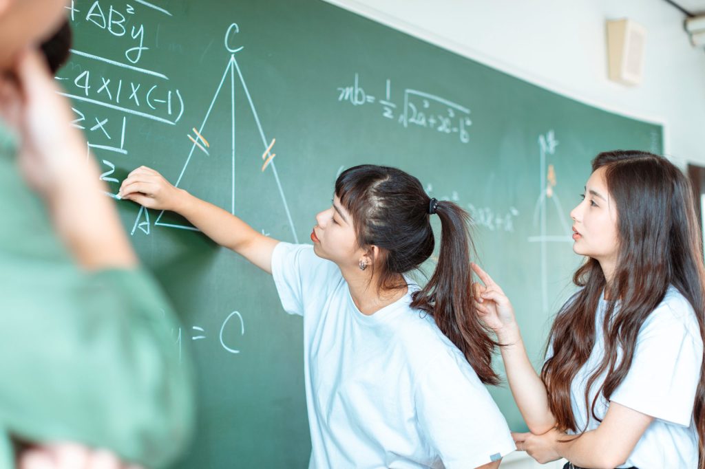 a student and teacher working on an algebraic problem on the board