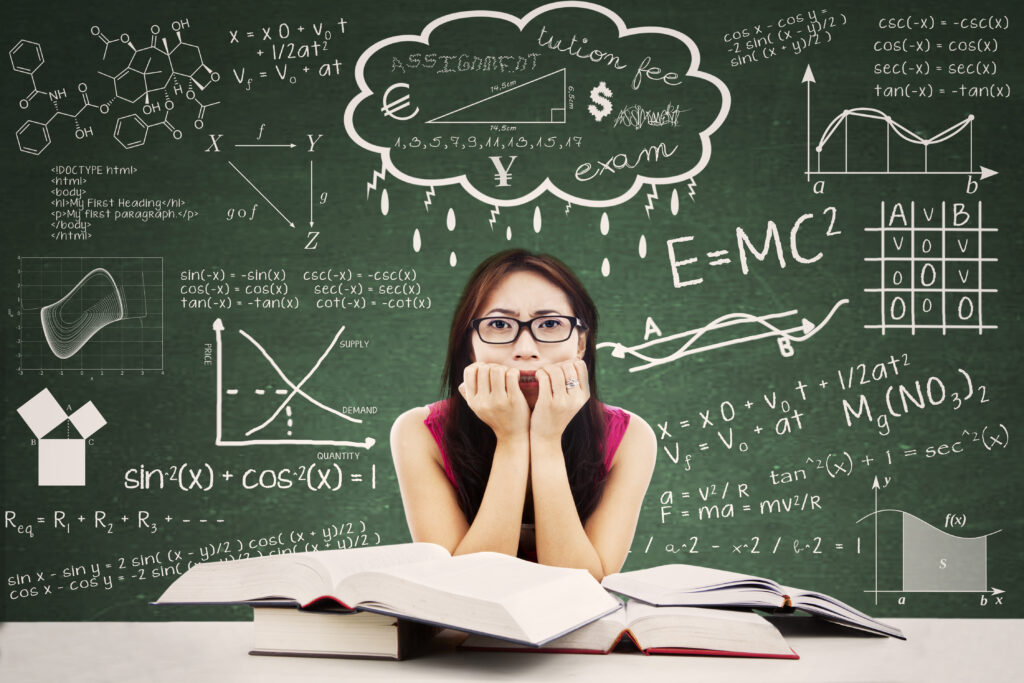 A stressed student sits at a desk with open books, biting her nails, surrounded by g3 additional math and science formulas, graphs, and equations drawn on a chalkboard background, with words like “assignment,” “exam,” and “tuition fee.”.