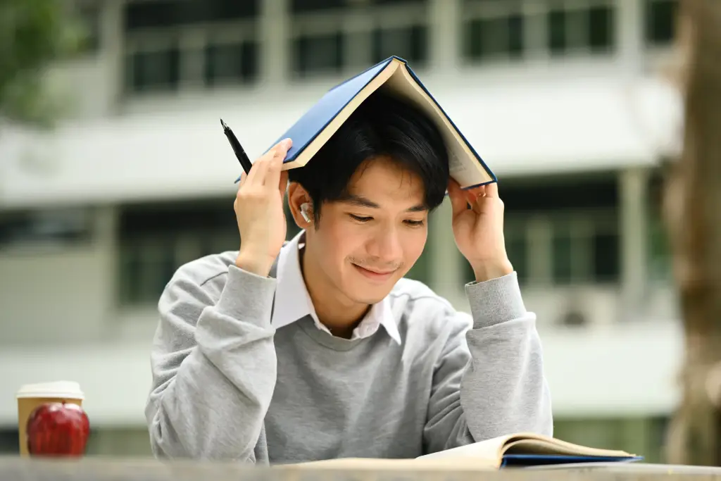 Happy Asian student balancing a book on his head, playful study portrait for education or campus content.