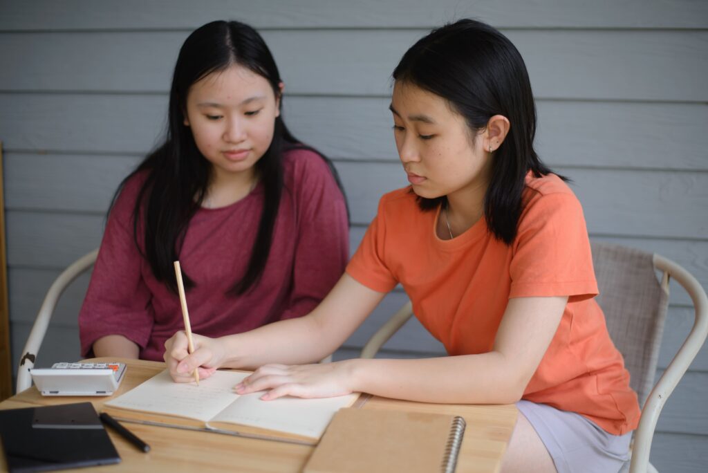 Two secondary school students working through A-Math practice questions together and reviewing their problem-solving methods.